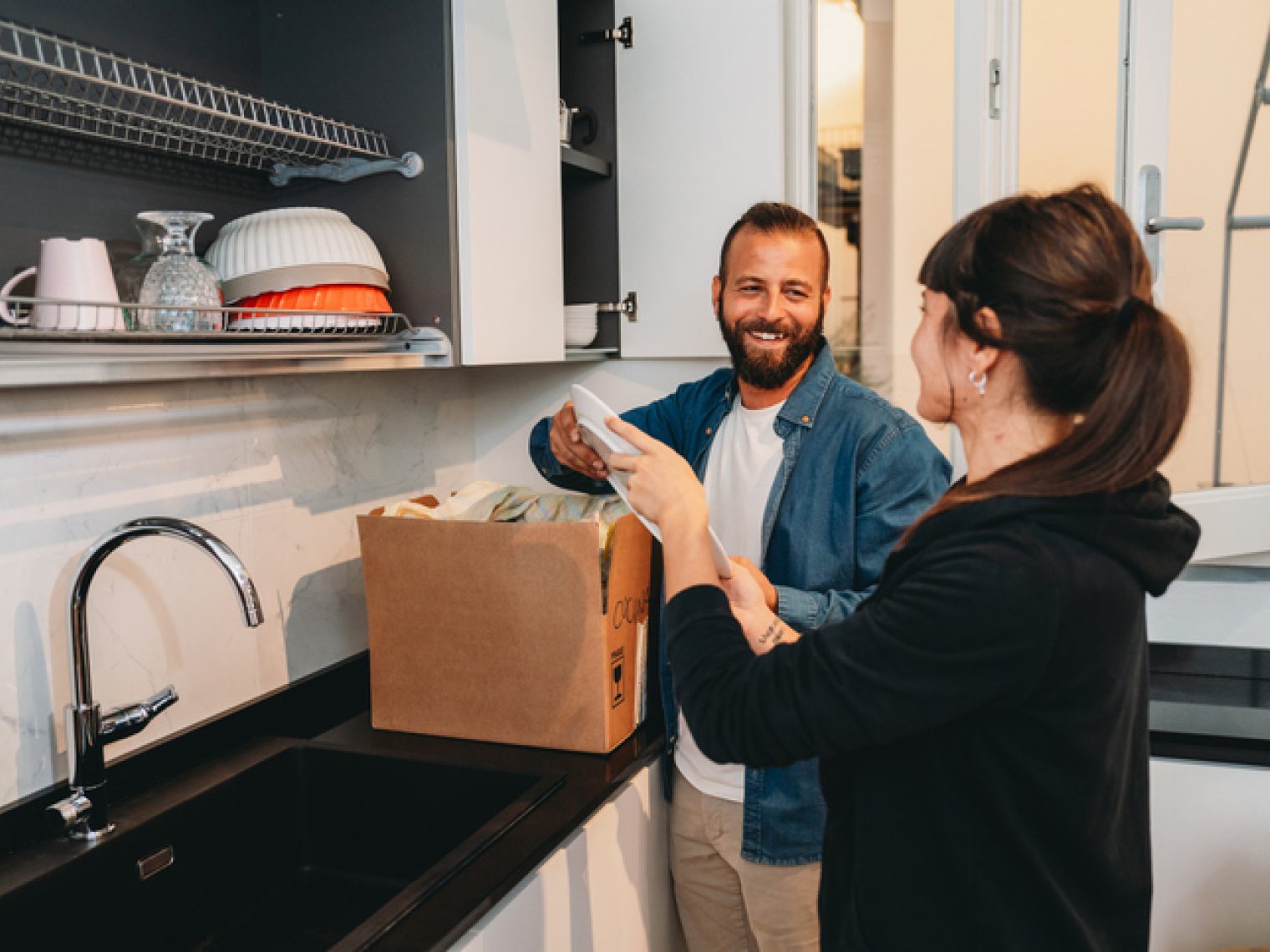 A man and woman are smiling and boxing items in a modern kitchen.