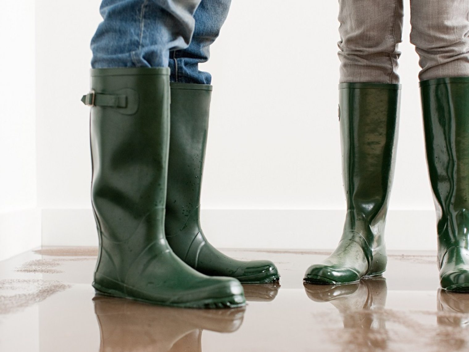 A couple wearing rainboots standing inside a flooded house.