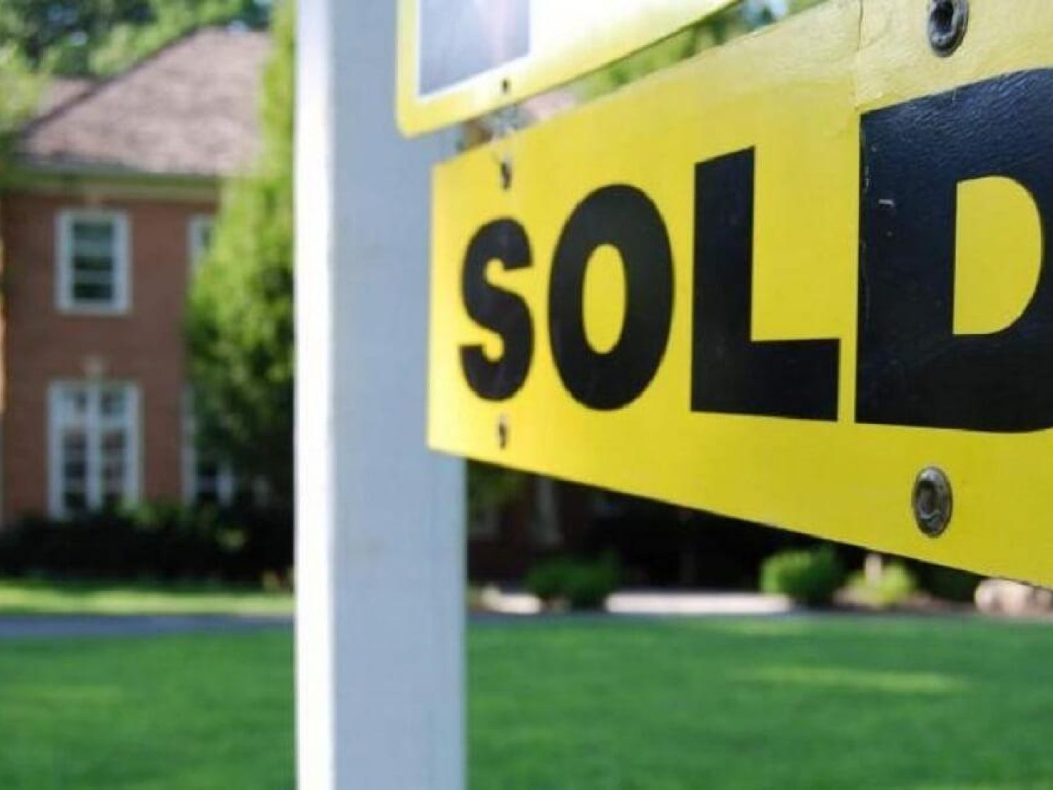 Closeup of a yellow and black sold sign in front of a house.