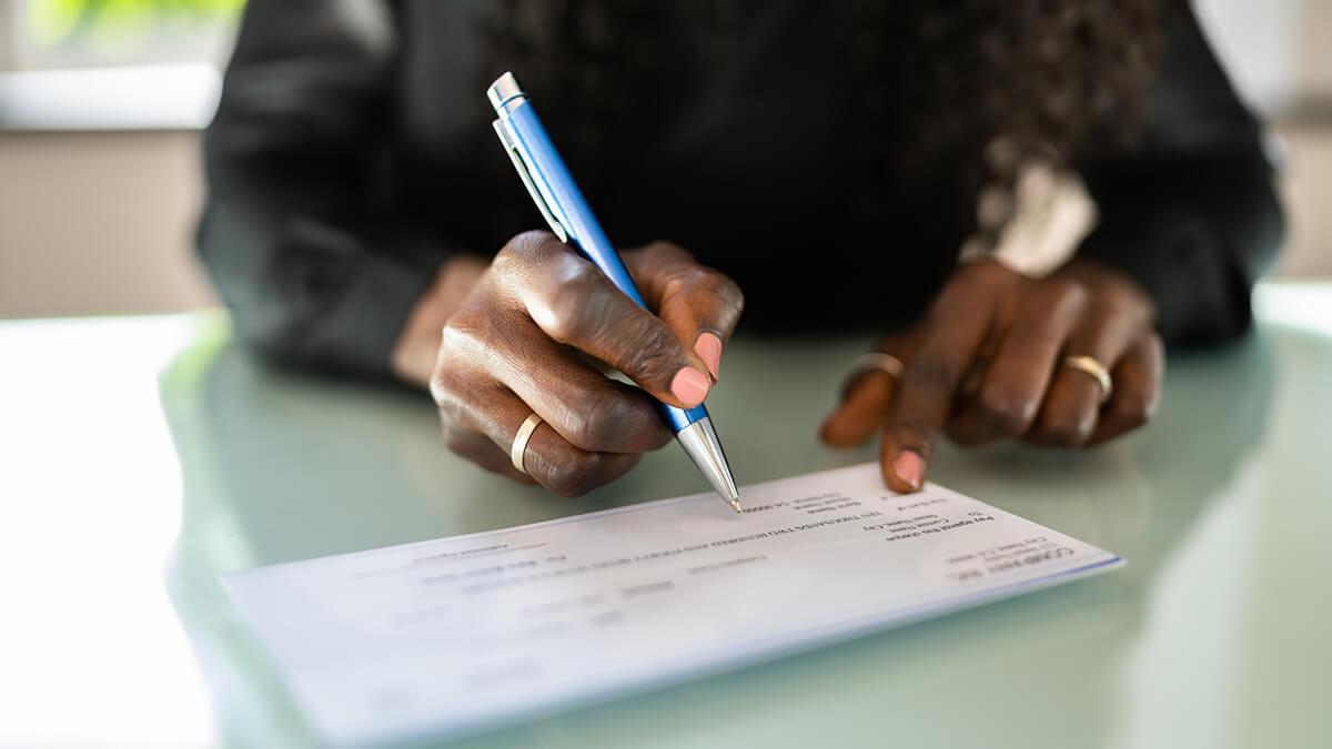 A man's hands prepare to write on a check with a gold pen.