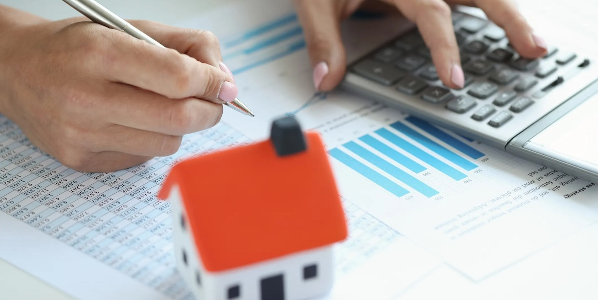 Person working with a calculator with a model of a home on the desk.